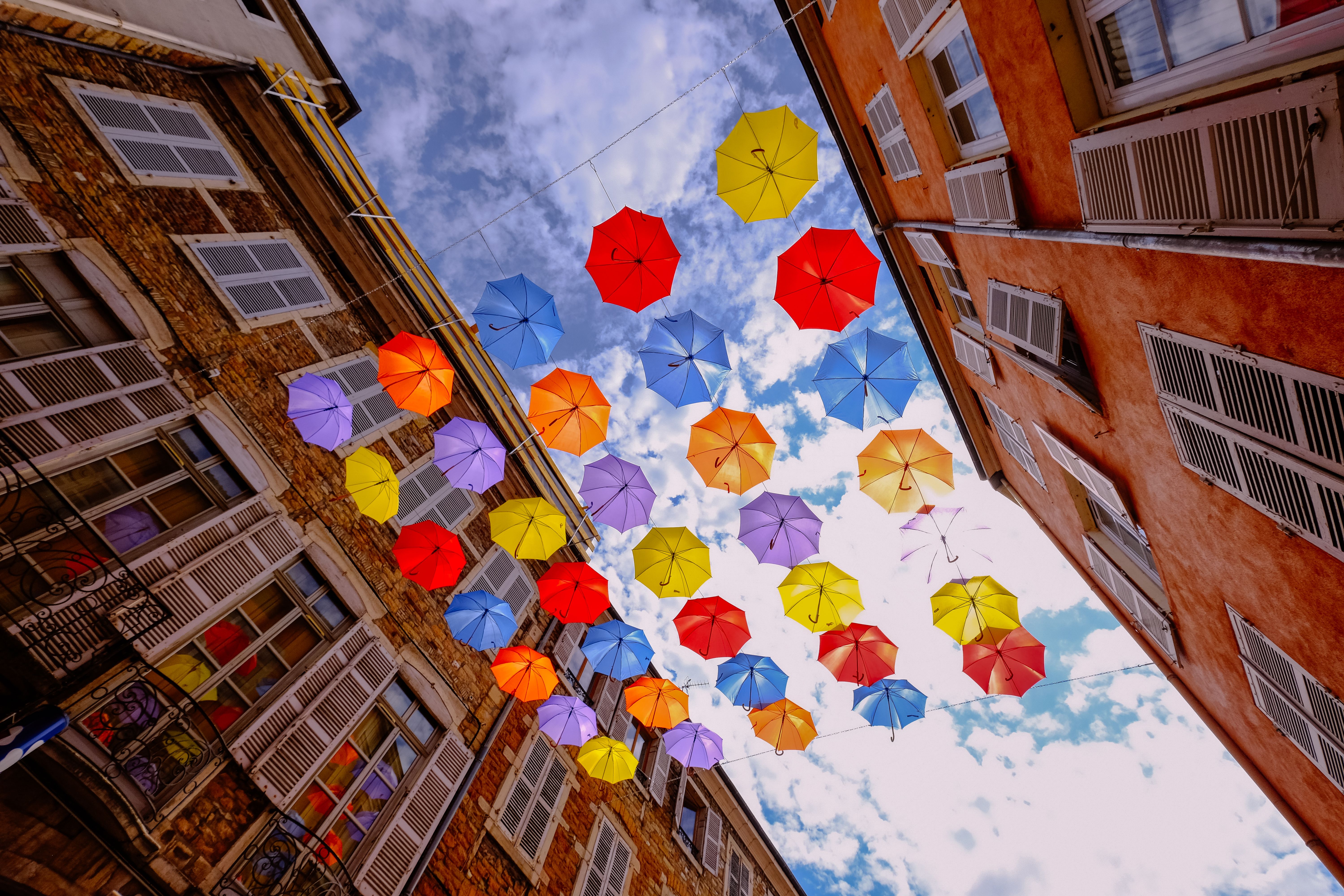 Rue d'un centre ancien animée par des parapluies colorés suspendus entre les façades